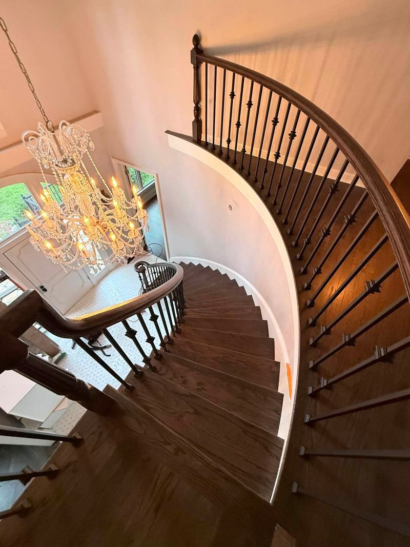 View down a curved staircase with dark treads and iron balusters