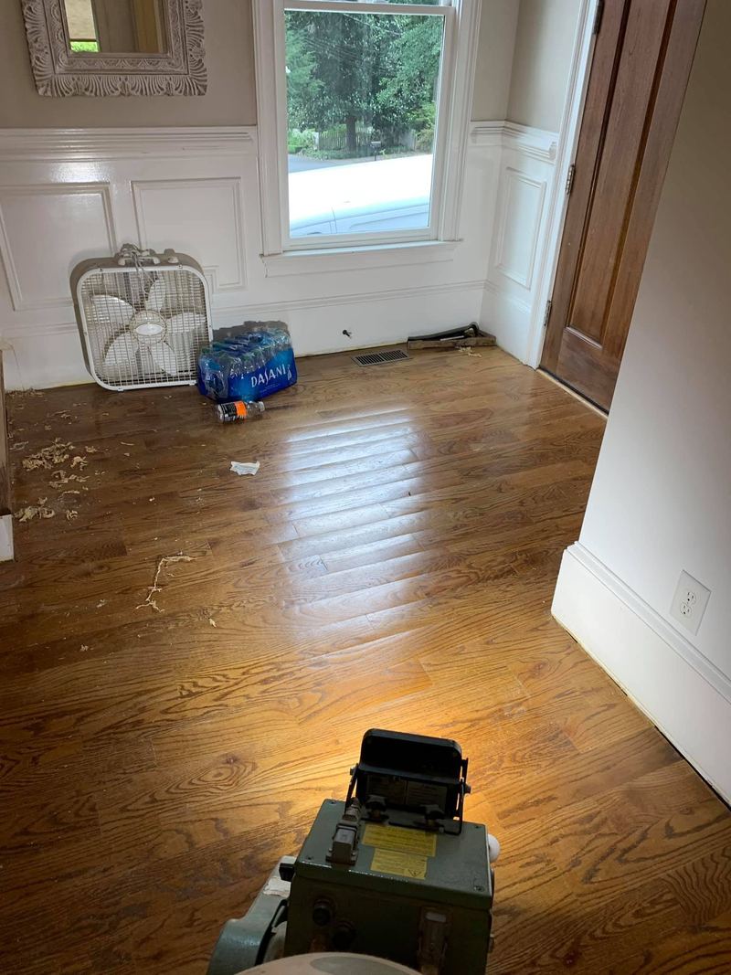 Worn oak floor with an edger in the foreground before sanding