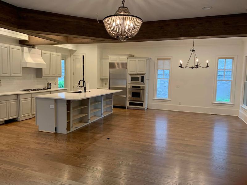 Open kitchen and dining area with a warm brown oak floor under a dark beamed ceiling