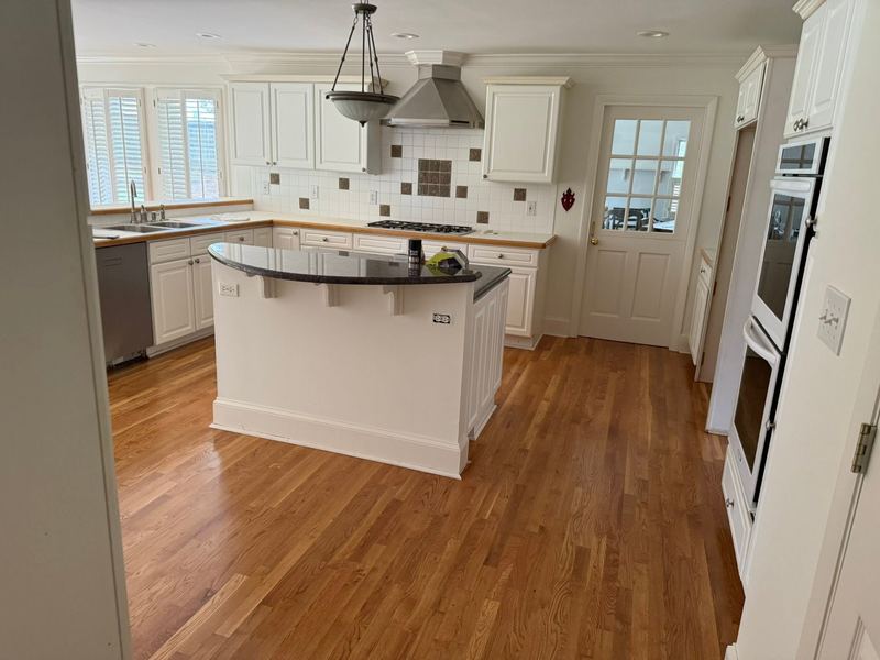 White kitchen with a curved island over a glossy red oak floor in a natural amber tone