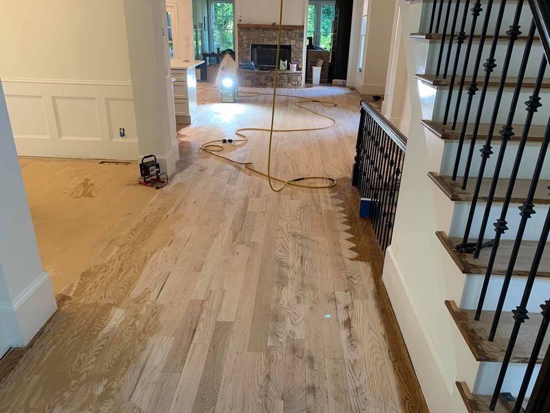 Open floor sanded to bare wood next to a staircase with iron balusters