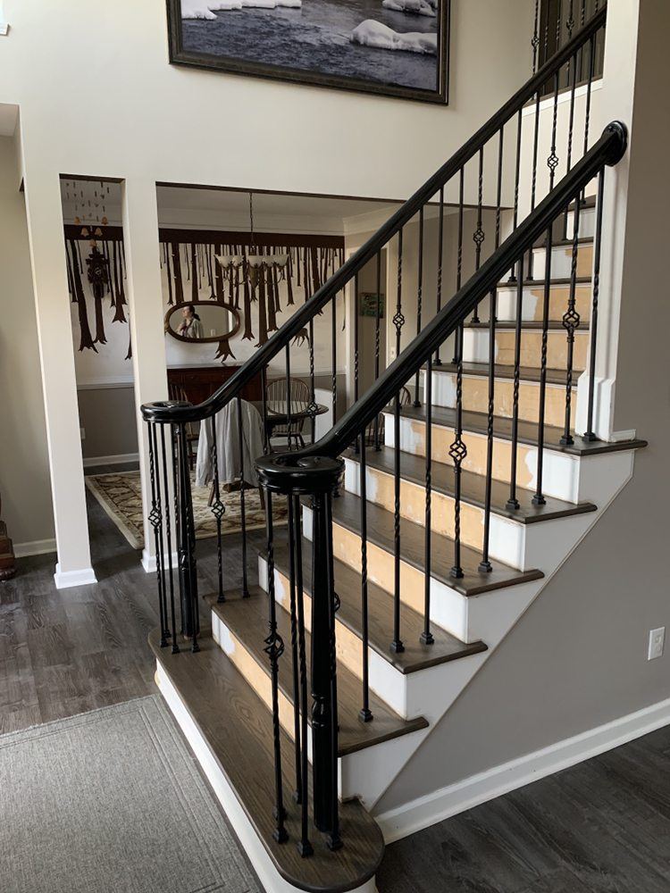 Staircase with gray stained treads, white risers, a black handrail and iron spindles